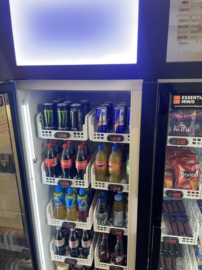 Smart fridge vending machine drinks selection close-up showing energy drinks and soft drinks with digital pricing