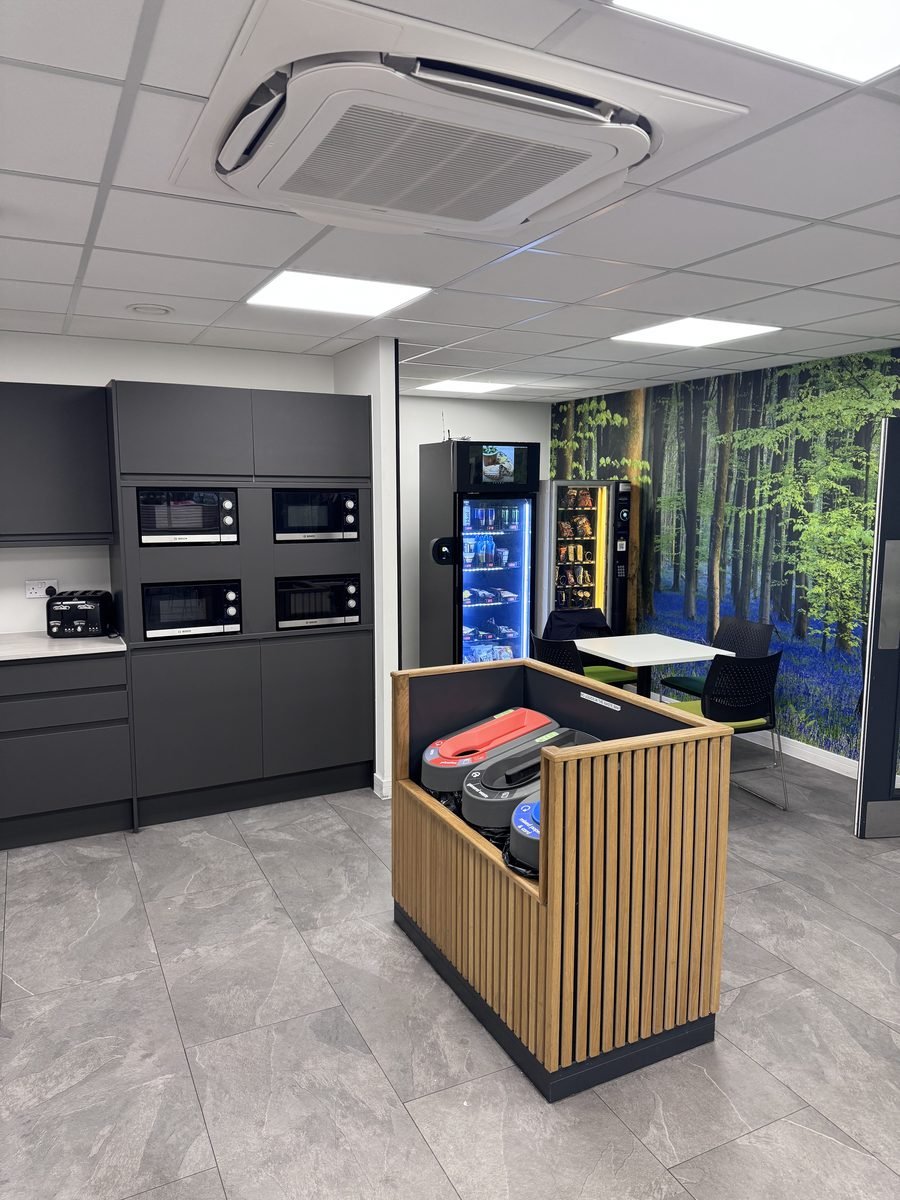 Free smart vending machine installed in modern workplace kitchen breakroom with microwaves and seating area